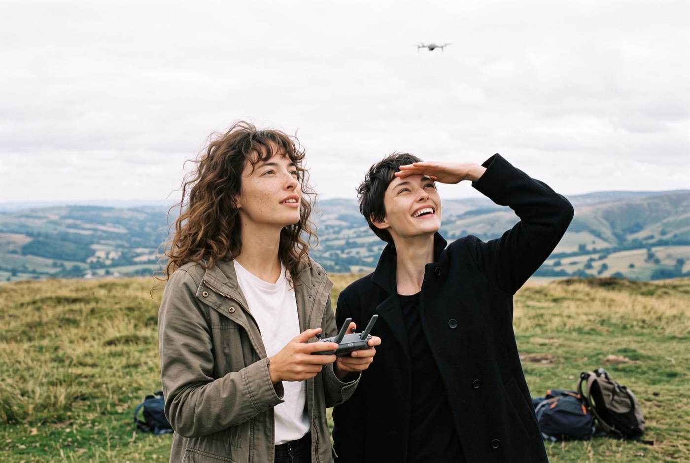Deux amies sur une colline, l'une pilote un drone qui vole au-dessus d'elles, l'autre le suit des yeux