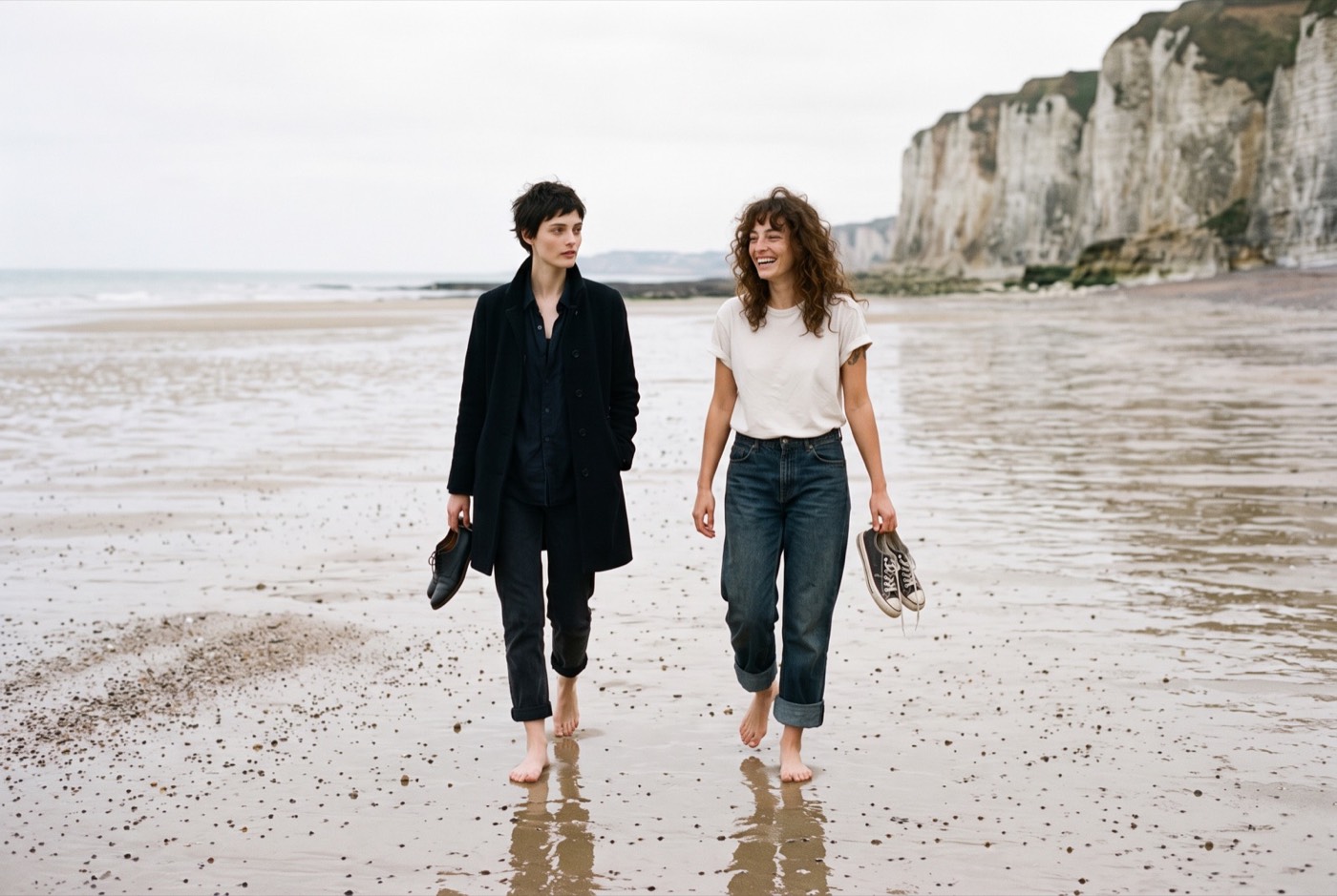Deux amies pieds nus sur la plage à marée basse, chaussures à la main, falaises de craie